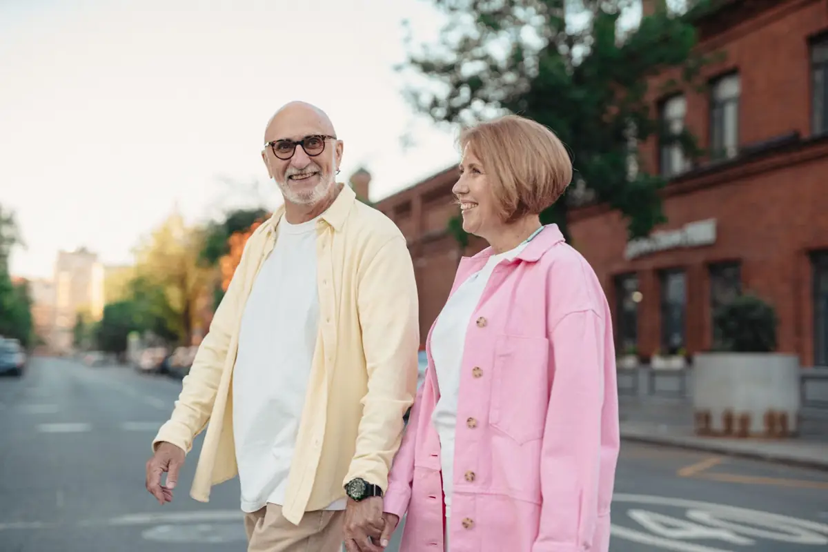 An older couple holding hands and smiling as they walk outdoors
